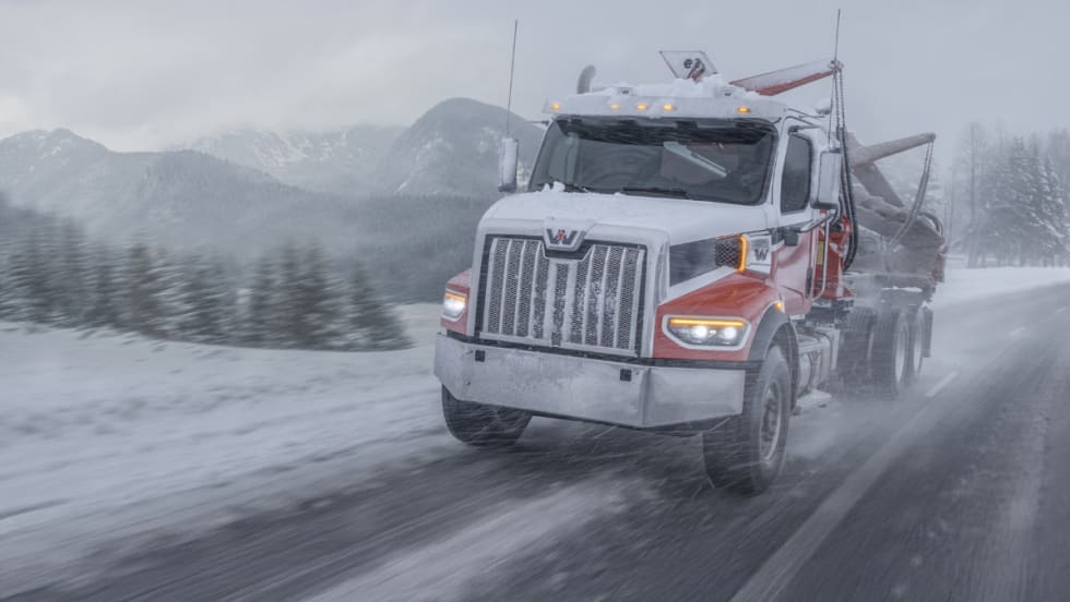 Western Star truck hauling logs through a snowy mountain road during a winter storm, highlighting extreme cold durability and performance testing.