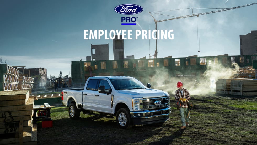 White Ford Super Duty pickup truck parked at a construction site beneath a Ford Pro Employee Pricing banner.
