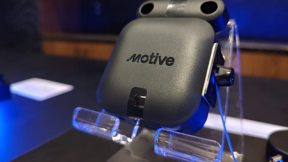 Close-up of a Motive-branded sensor device displayed on a clear stand under blue lighting, likely used for fleet monitoring or environmental and door tracking applications.