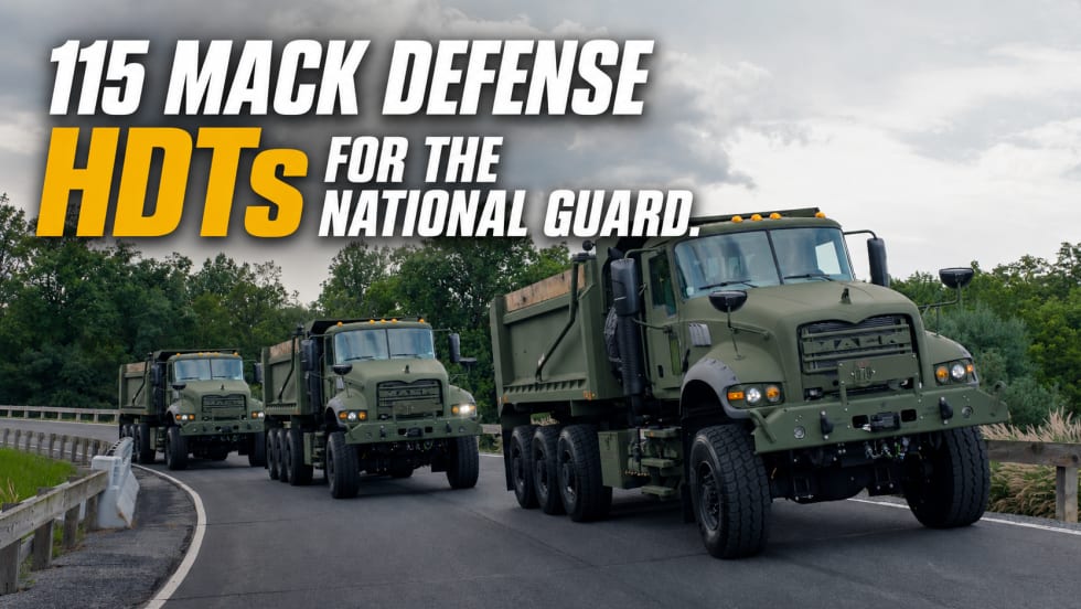 Three olive-drab Mack Defense heavy-duty tactical dump trucks drive in convoy on a roadway beneath cloudy skies, promoting delivery of 115 HDTs for the U.S. National Guard.