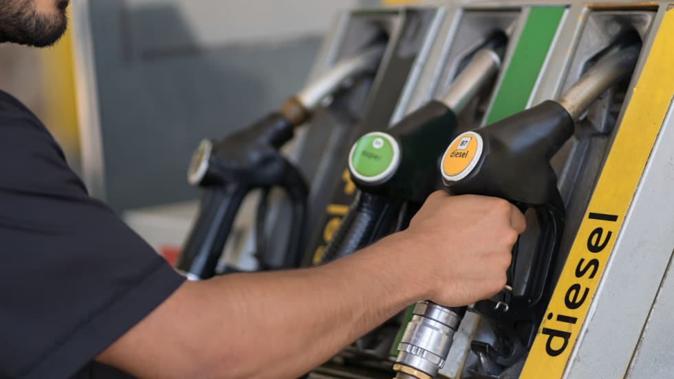 A worker reaches for a B7 diesel fuel nozzle at a commercial fueling station with several fuel options.