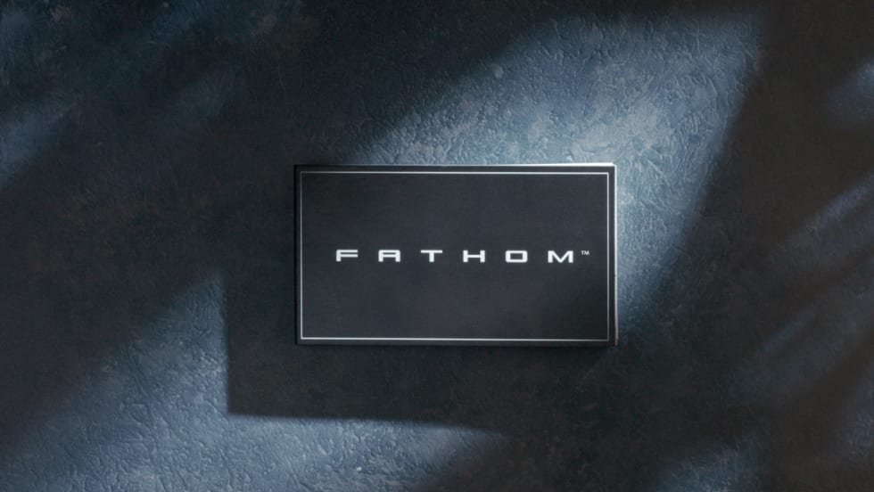 Black Fathom nameplate mounted on a dark textured wall, illuminated by soft directional lighting that creates subtle highlights and shadows, emphasizing the brand’s minimalist, modern aesthetic.