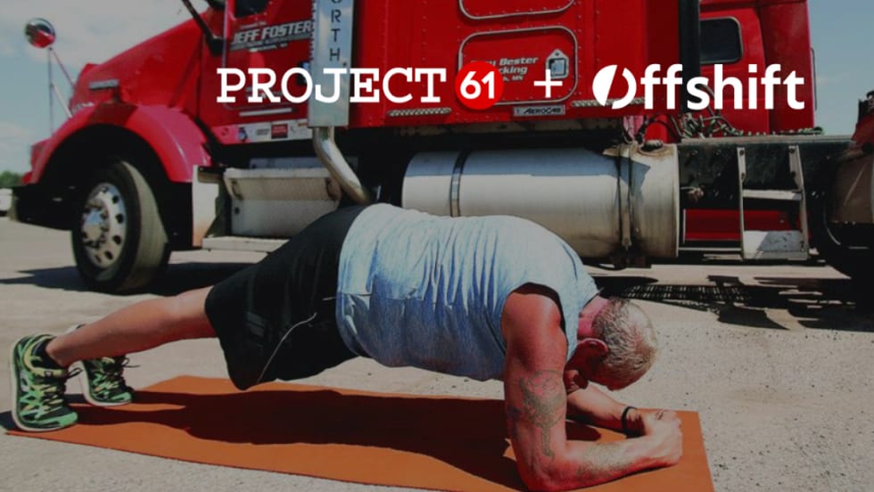 Truck driver doing a plank exercise on a mat with a red truck in the background.