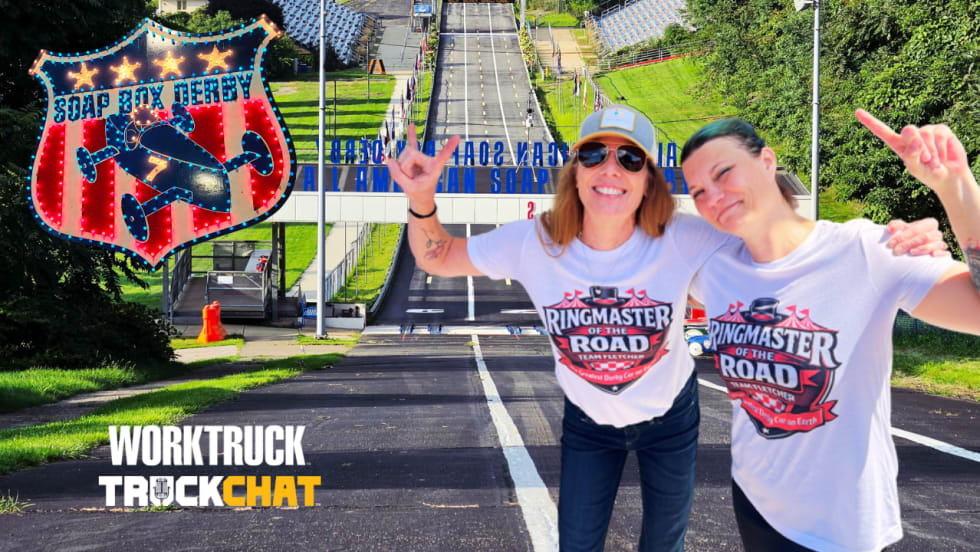 Lauren Fletcher and Kim Davidson pose at Derby Downs with the All-American Soap Box Derby track behind them, alongside Soap Box Derby and Work Truck Truck Chat graphics.