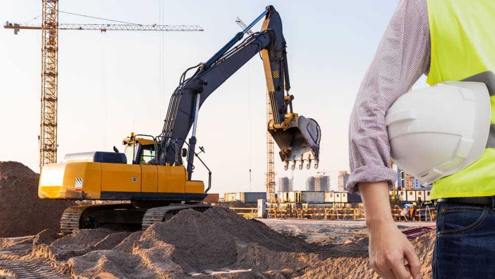 Construction site in background with worker and hard hat in foreground.