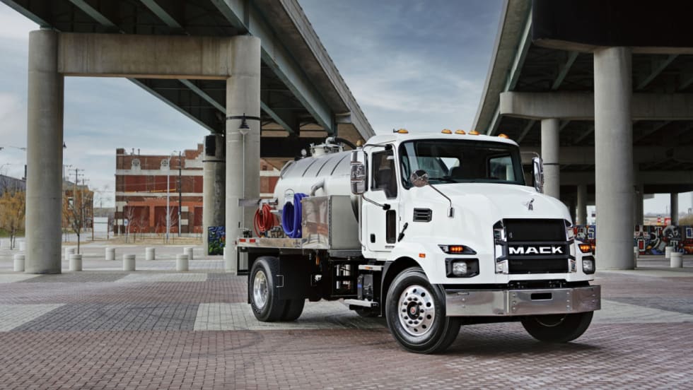 White Mack MD medium-duty vocational truck equipped with a tank body parked beneath an overpass.