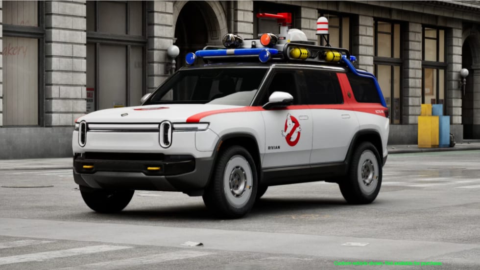 White Rivian R1S SUV customized as the Ghostbusters Ecto-R1, featuring the Ghostbusters logo, red accents, roof-mounted equipment, and emergency-style lights.