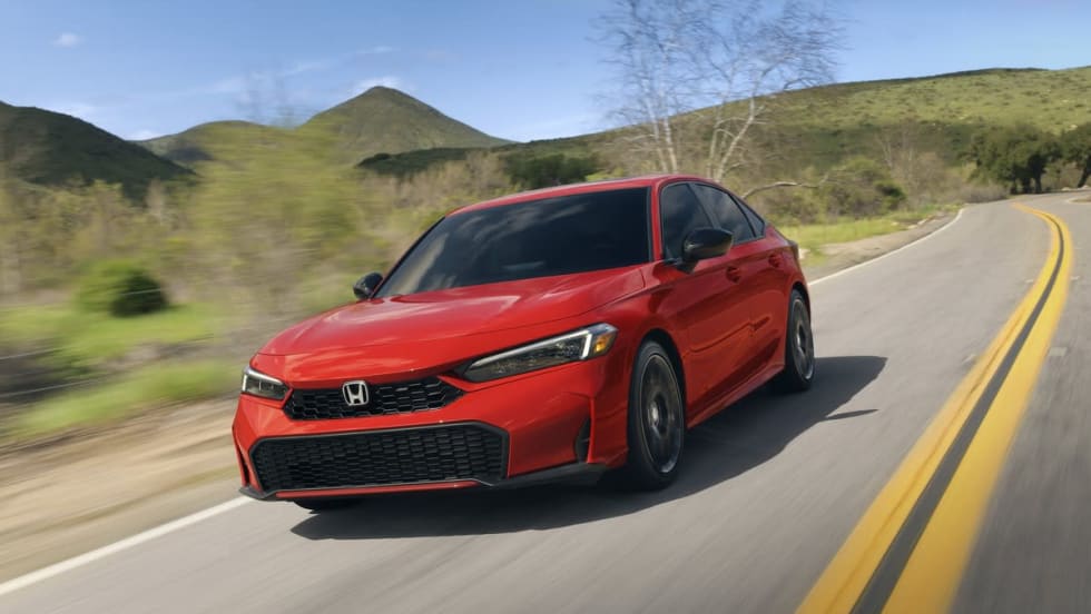 Red Honda Civic hybrid sedan on two lane road with green hills in background