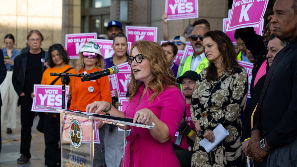 Supervisor and LA Metro Board Member Lindsey P. Horvath stands at a podium with a crowd of community members behind her.