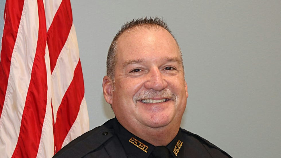 Smiling police officer in black uniform standing in front of American flag