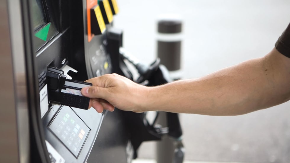 Person inserting a payment card into a fuel pump card reader at a gas station