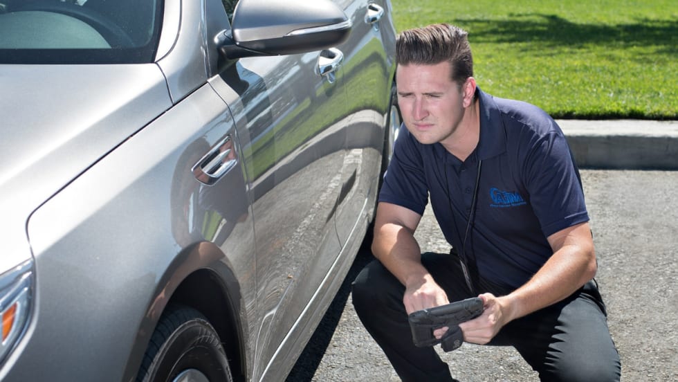 Vehicle inspector looking down the left side of a gray vehicle for any damage.