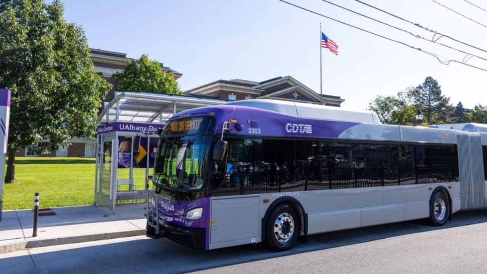 A purple and white CDTA bus parked at a bus stop.