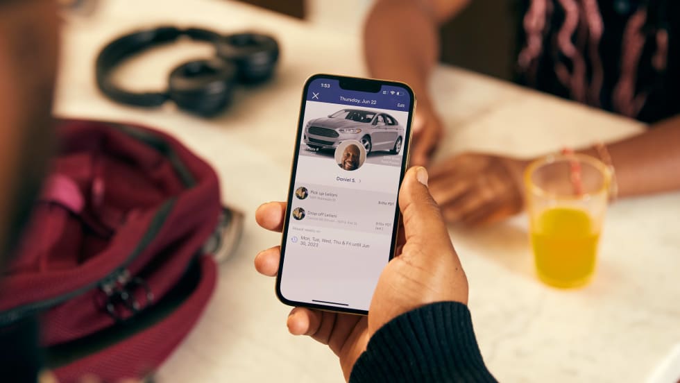 A close up image of a hand holding a phone with HopSkipDrive's platform and CareDriver information on the screen.