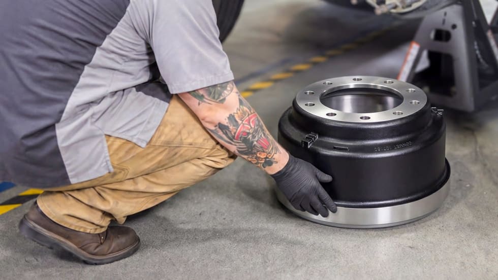 Heavy duty truck technician crouched down replacing brake drum