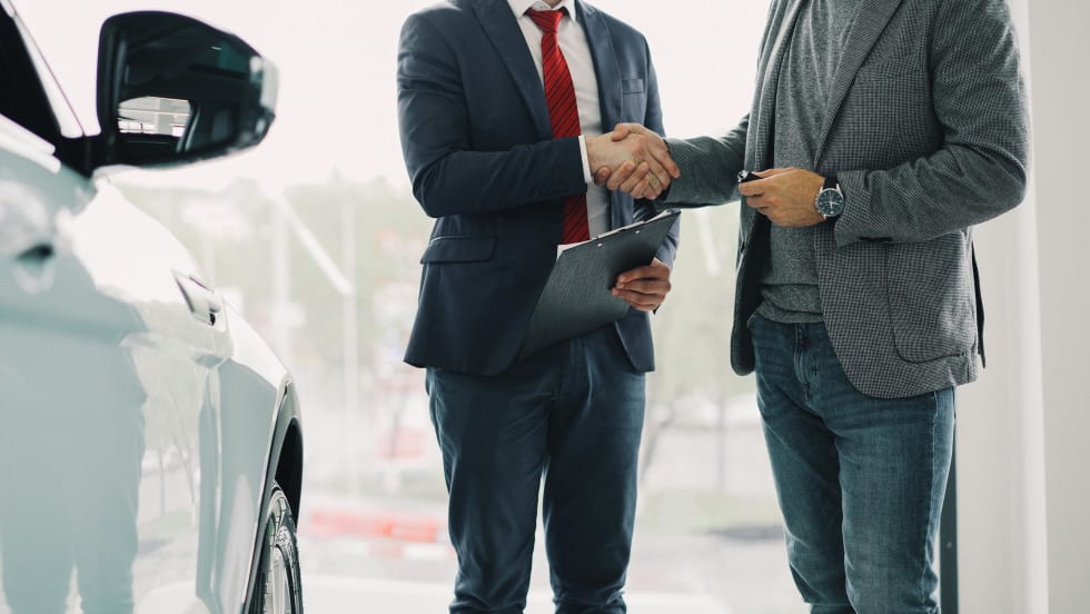 Photo of two businessmen shaking hands next to a white car in a showroom