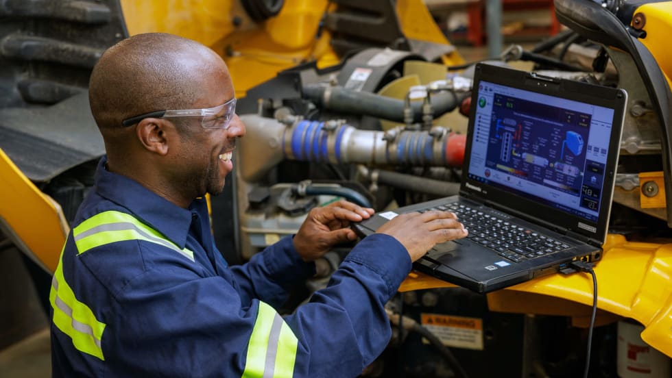Technician using a laptop to diagnose and service a school bus engine, highlighting fleet maintenance technology and transportation operations.
