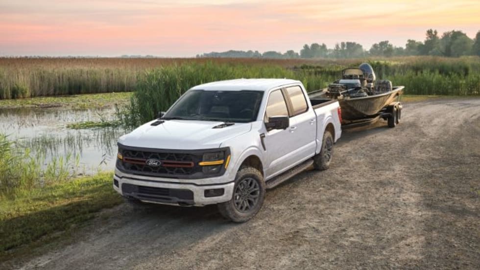 Photo of white Ford F-10 pickup parked on a dirtl road next to a body of water and with a fishing boat hitched to it