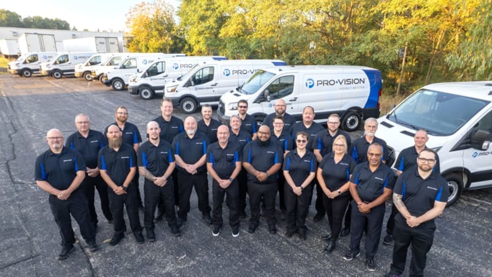 a line of pro-vision employees stand in front of branded company vans 