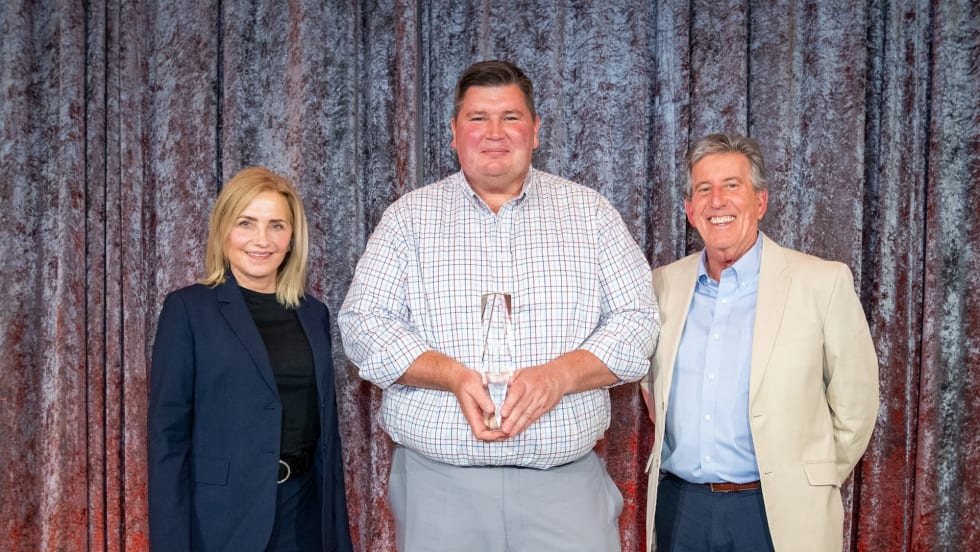A photo of three people holding a trophy on a stage
