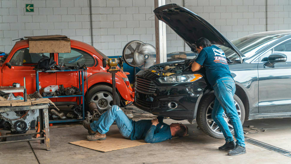 Two men do mechanical work on car.