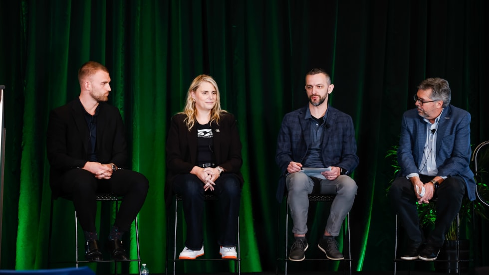 Three men and one woman sitting on a green backlit stage talking