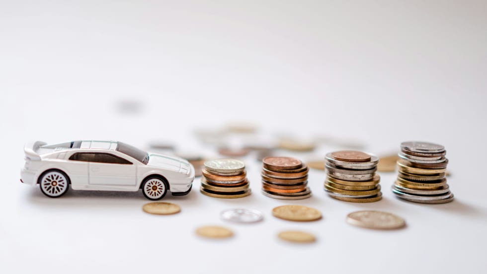 Tiny toy car in front of small stacks of coins