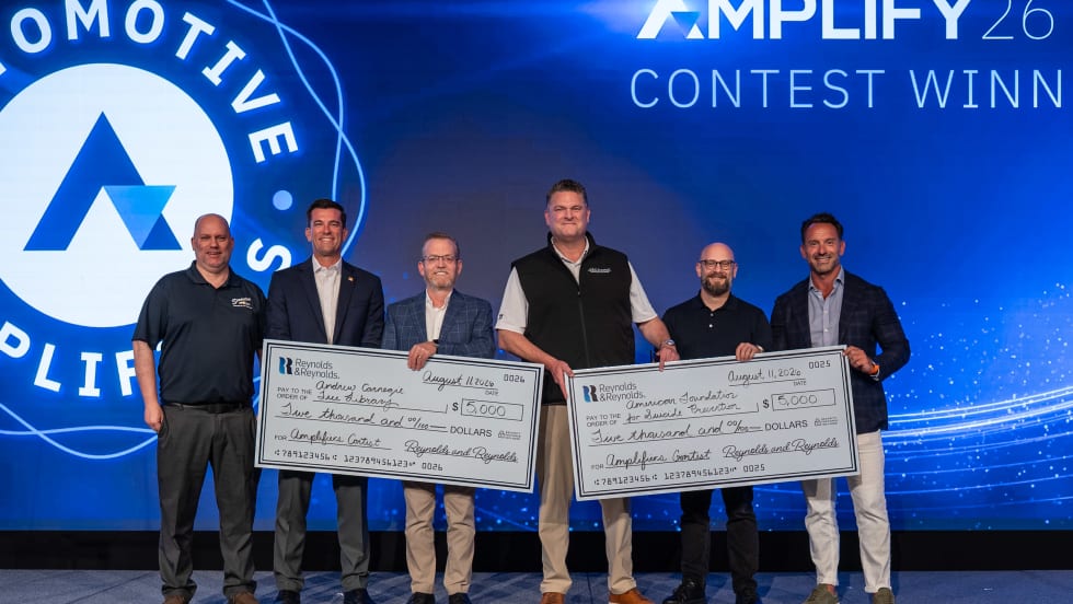 Six men standing on stage receiving two giant $5,000 checks.