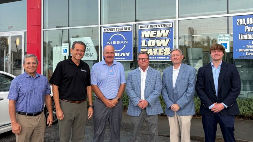 Six men standing for photo outside of car dealership