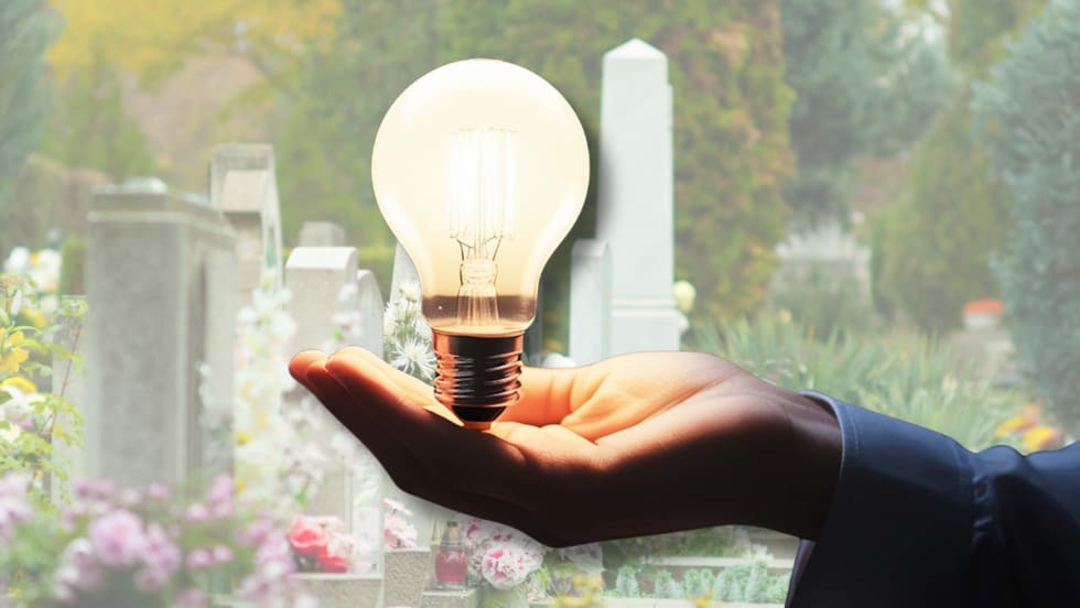 Illustration of a hand holding a light bulb against the background of a cemetery