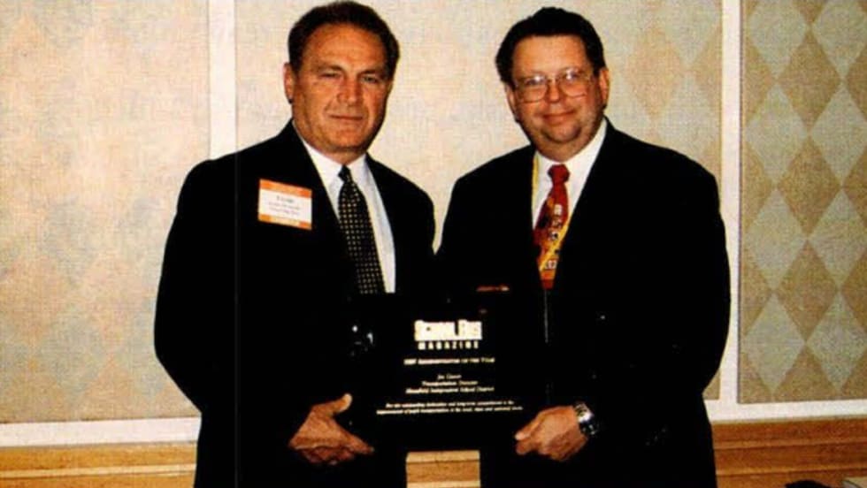 two men in black suits stand together for an award presentation