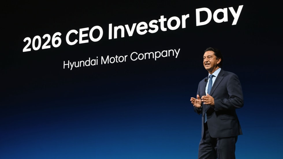 Businessman in a suit speaking on stage at an event with '2026 CEO Investor Day' displayed in background