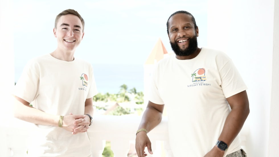 two men stand next to each other in white t-shirts