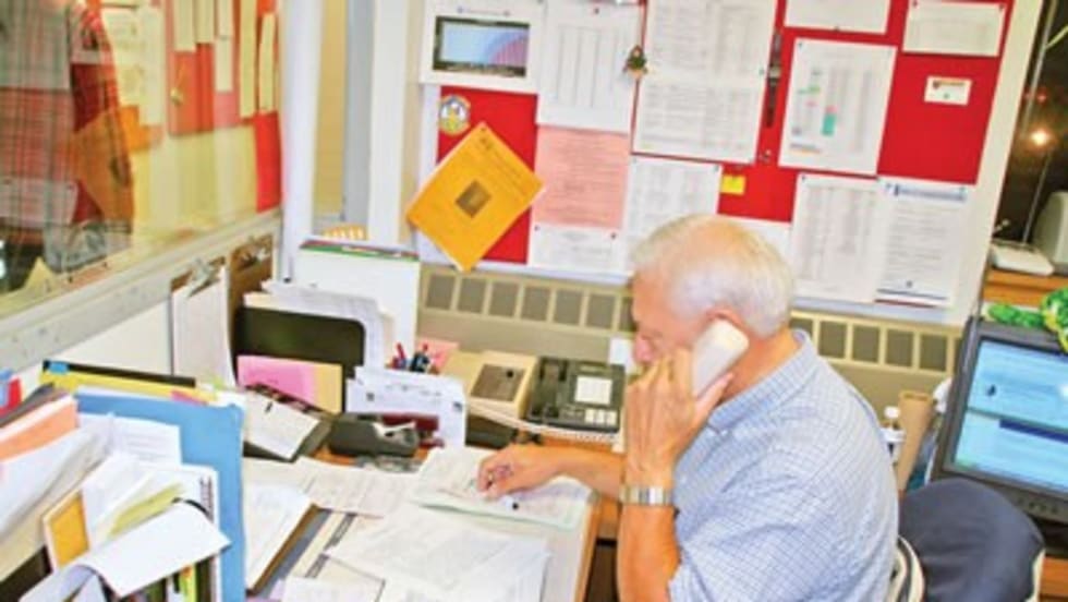 a man sits at a desk full of paperwork while on the phone