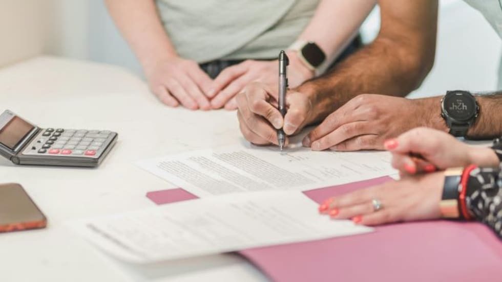 Three people's hands on desk as one signs a document