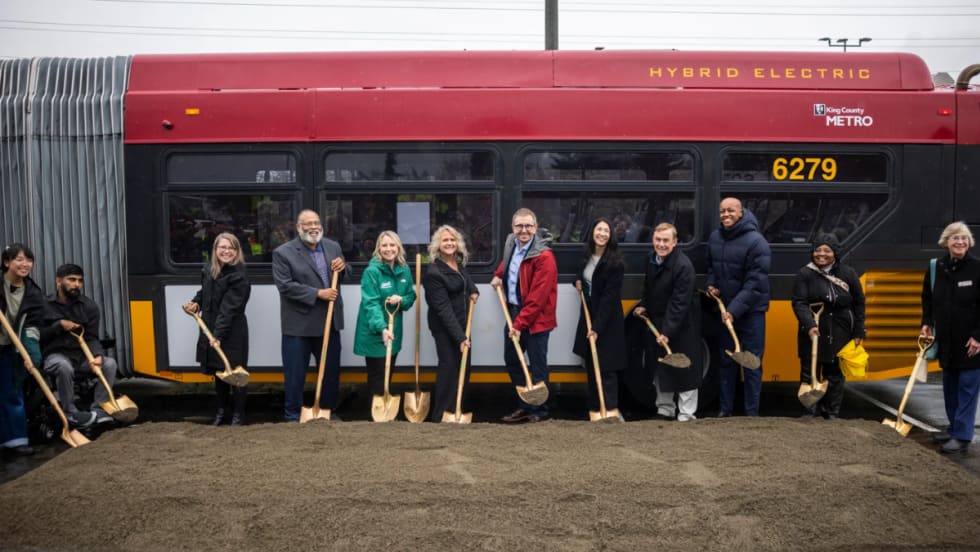 County and agency officials break ground in front of a red and yellow King County Metro public transit bus.