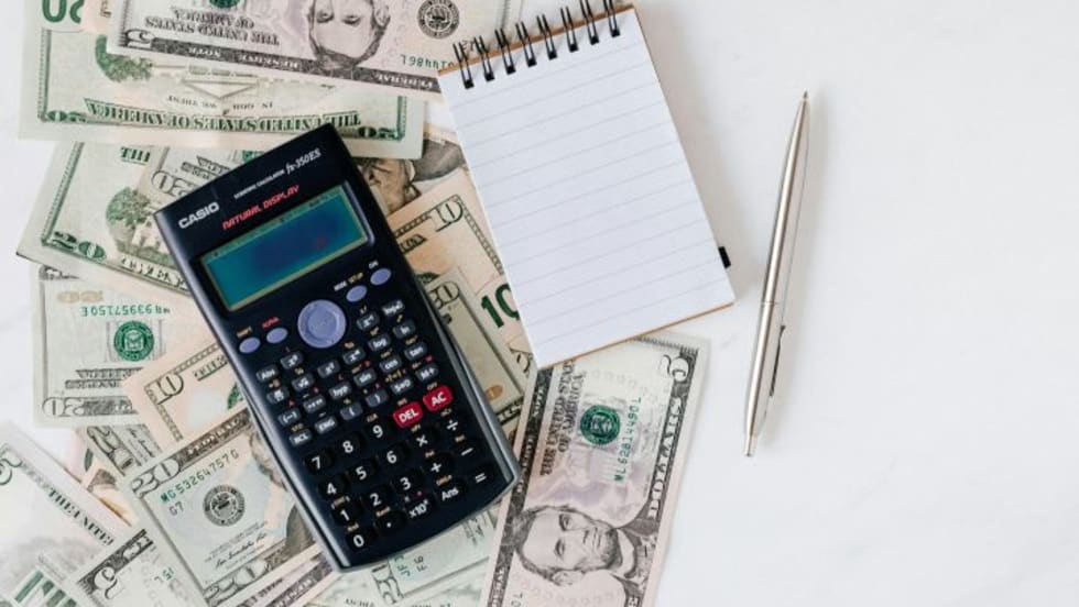 Photo of paper money bills, a calculator, notepad and pen
