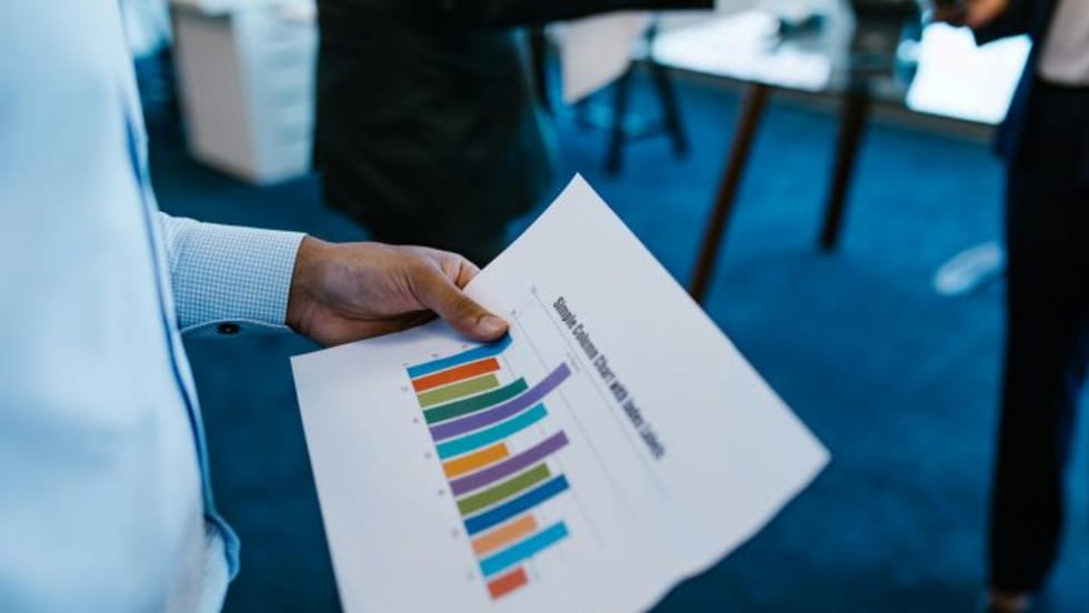 Man's hand holding paper with bar chart on it