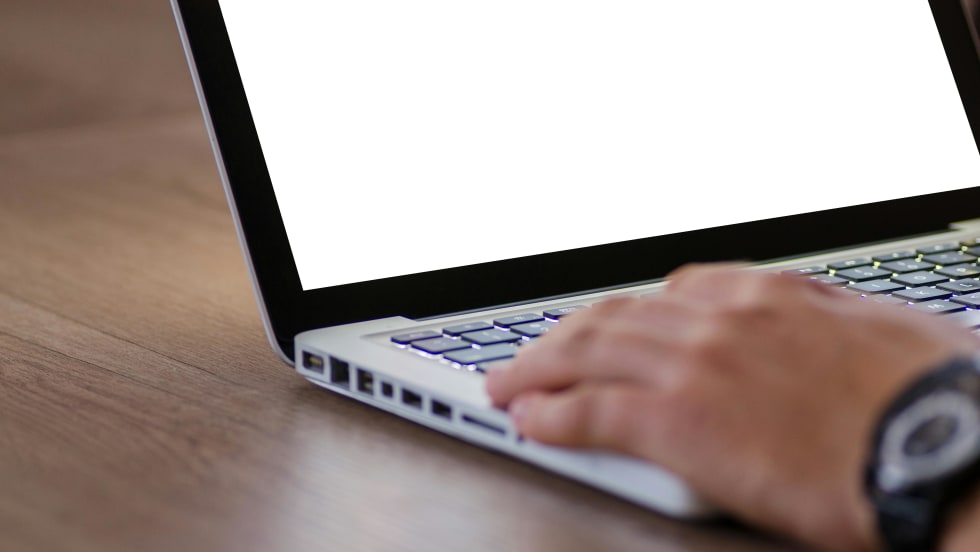 Photo of man's hand on laptop computer keyboard with blank screen