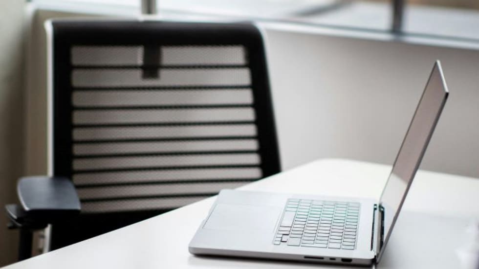 Laptop computer open on desk with empty chair behind it
