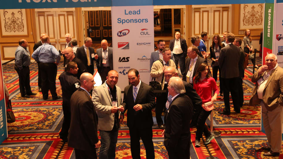  Attendees networking and talking in a conference hall beneath signage for the Industry Summit with sponsor displays in the background.