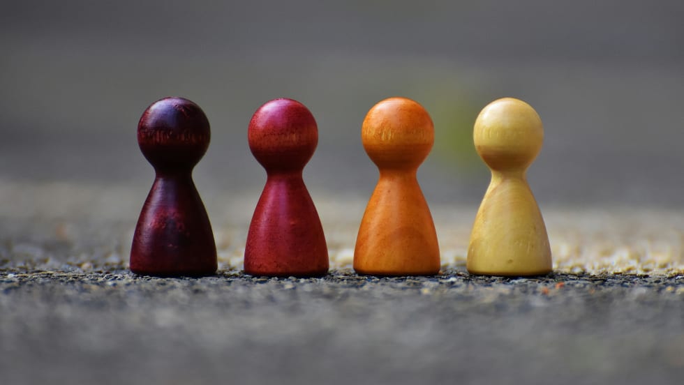Wooden people figures of different colors in a row, similar to board game pieces