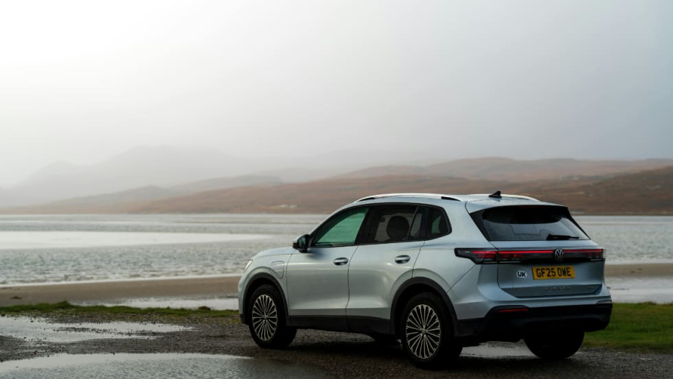 white SUV parked in front of a body of water with a gray sky background