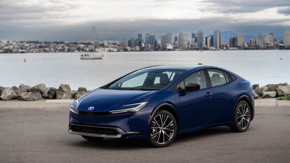 Photo of blue Toyota Prius parked next to a body of water with a city skyline behind it