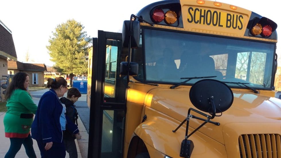 three people board a school bus