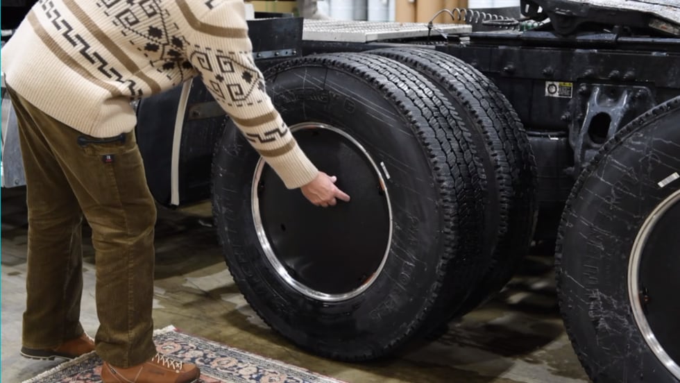 Dual truck tires with black aerodynamic wheel cover and a man bending down getting ready to take one off