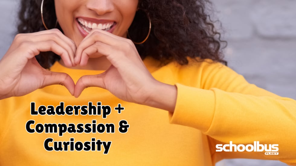 A smiling person in a yellow sweater forms a heart shape with their hands above the words "Leadership + Compassion & Curiosity." The graphic accompanies a School Bus Fleet feature on how empathy, compassion, and curiosity can strengthen leadership in student transportation.