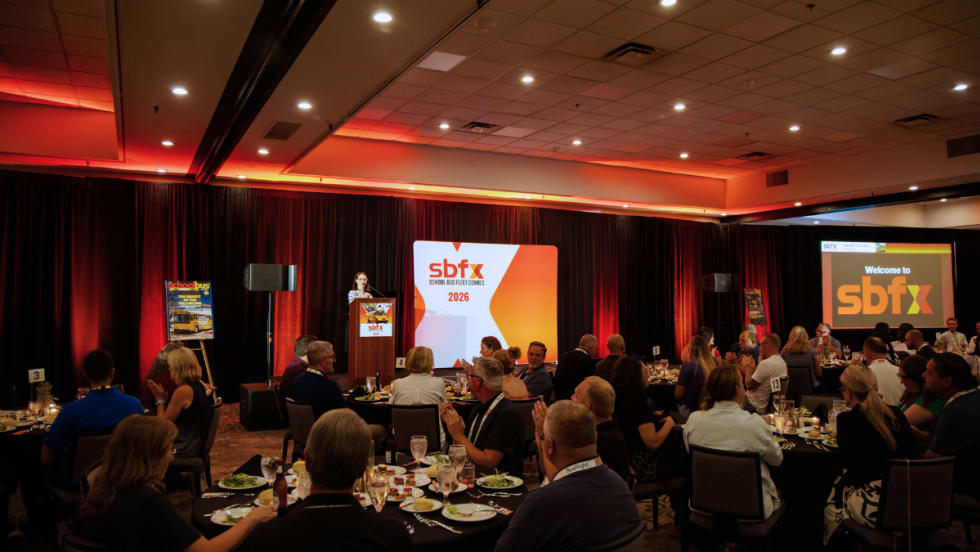 Attendees seated at banquet tables during a School Bus Fleet ConneX 2026 event, with a speaker at the podium and SBFX signage onstage.