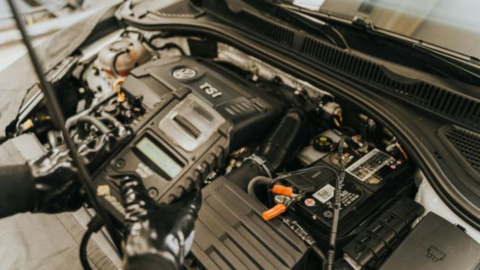 Mechanic holding a vehicle diagnostic device while standing above an open car hood