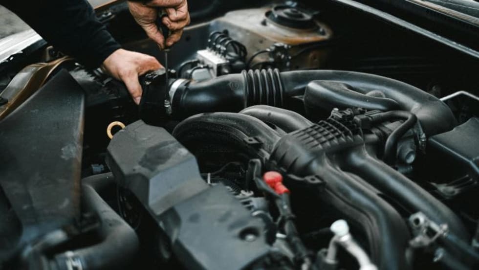 Photo of man working under the hood of a car with a tool